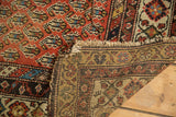 Antique Hamadan rug's folded corner reveals hand-knotted back, allover boteh pattern, and tattered fringe.