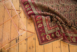 Folded Antique Karabagh carpet revealing wine red border, ivory boteh patterns, and dark field.