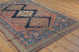 Corner of antique Persian Afshar rug displaying dense teal, blush, ivory floral motifs and tattered fringe.