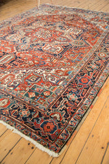 Corner of vintage Heriz carpet showing geometric navy border, red field, and polychrome selvage.