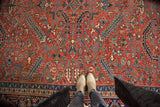 Vintage Heriz carpet's brick red field with geometric florals and tendrils, viewed from above with feet.