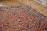 Vintage Heriz rug's brick red field with serrated leaves, geometric tendrils, and navy border.