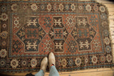 Geometric crab motifs and tribal borders on a madder red antique Caucasian rug, showing storied wear.
