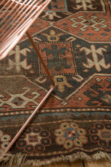 Worn fringed edge of the hand-knotted antique Caucasian rug, showing geometric madder red motifs.
