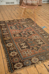 Tattered fringe and worn geometric 'crab' motifs on antique Caucasian rug corner.