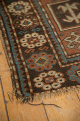 Antique Caucasian rug corner with tattered fringe, geometric patterns in madder red, ivory, teal.