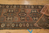 Antique Caucasian rug's worn geometric crab patterns, floral border, teal, rust, ivory tones.