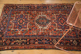 Karaja rug detail: brick red field with dense pinwheel florals and navy geometric border.
