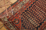 Antique Hamadan rug's madder red border, floral corner spandrel, and navy boteh field.