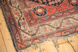 Antique Hamadan rug corner shows worn madder red border with meandering vine, tattered fringe.