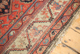 Antique Hamadan rug detail: European-style meandering border, worn madder red field, and frayed end.