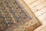Antique Kurdish rug corner: worn navy field with henna motif, red, celadon borders, tattered edge.