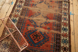 Visible foundation and textured wear on an antique Caucasian rug with brick red and navy patterns.