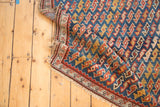 Antique Caucasian rug fold: indigo, red, yellow geometric serpent motif with tattered fringe.