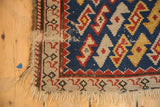 Antique Caucasian rug corner with tattered fringe, beige border, and indigo serpent motif.