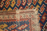 Antique Caucasian rug corner: blue, red geometric pile, beige foundation, and tattered fringe.