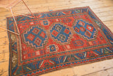 Antique Caucasian rug corner detail: red field, abstract motifs, blue border, and light etching.