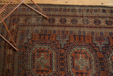 Detailed geometric borders and patterns of an antique Belouch rug in copper, navy, ivory.
