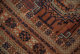 Layered geometric borders with intricate copper, navy, and ivory patterns on an antique Belouch rug.