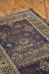 Antique Belouch rug corner showing geometric guls, navy blue, madder red, and beige.