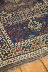 Antique Belouch rug corner, detailing geometric guls, rich navy, madder red, and tattered fringe.