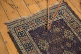 Antique Belouch rug corner displays geometric guls in navy, madder red, ivory, and tattered fringe.