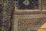 Antique Belouch rug corner, featuring geometric guls in navy, madder, and beige with tattered fringe.