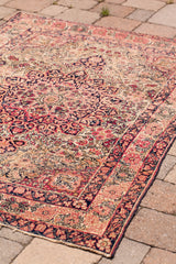 Section of antique Kerman rug, showing blanched traditional floral motifs in muted red, navy, and cream.