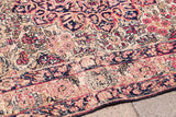 Textured detail of an antique Persian Kerman rug's blanched floral pattern and worn edge.