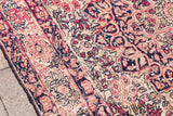 Worn Kerman rug corner, blanched ivory ground, muted red and indigo curvilinear patterns.