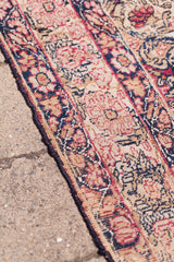 Antique Kerman rug showing blanched red and deep blue motifs on its worn side edge.