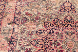 Textural close-up of worn antique Kerman rug showing blanched red and blue floral motifs.