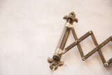 Decorative fleur de lis bracket and distressed accordion arm of the antique shaving mirror.