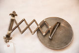 Detail of antique shaving mirror's circular metal back, accordion arm, and aged finish.
