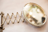 Aged oval beveled glass shaving mirror with visible lines and accordion arm patina.