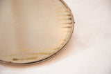 Oval antique shaving mirror detail with time-softened discoloration on glass and metal frame.