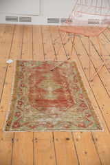 Distressed Oushak rug corner, faded red and green border, showing stylized plant motifs and wear.