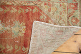 Corner of distressed Oushak rug, faded red pile, visible knot heads, fringe, and hand-knotted reverse.