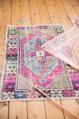 Distressed vintage Oushak rug corner showing worn pink, blue geometric patterns and fringe.