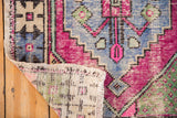 Distressed Oushak rug corner showing bright pink, blue, and green geometric pattern with woven backing.