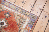Distressed Oushak rug corner, faded cherry red and pale blue, with visible foundation showing through.