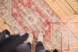 Vintage distressed Oushak runner featuring cherry red, ivory, and muted green patterns.