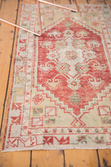Distressed vintage Oushak rug runner's lower corner, revealing cherry red and ivory patterns.