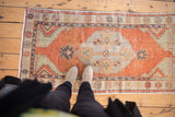 Distressed vintage Oushak runner in faded brick red, antique ivory, and soft grey with even wear.