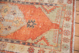 Vintage distressed Oushak runner's faded brick red field, stylized ivory borders, worn pile, and fringe.