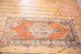 Geometric patterns and simplistic flowers on distressed Oushak rug corner in faded brick red and beige.