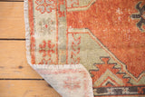 Distressed Oushak rug corner, faded brick red pile, primitive pattern, and visible foundation.