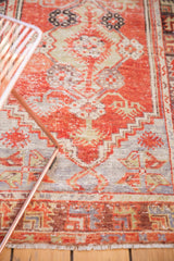 Detail of a distressed Oushak rug with cherry red field, stepped chocolate brown border, and fringe.