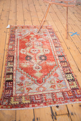 Distressed vintage Oushak rug corner features cherry red, vine border, and fringed edge.