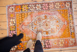 Textured distressed Oushak rug featuring vivid tangerine and saffron hues and floral medallion.